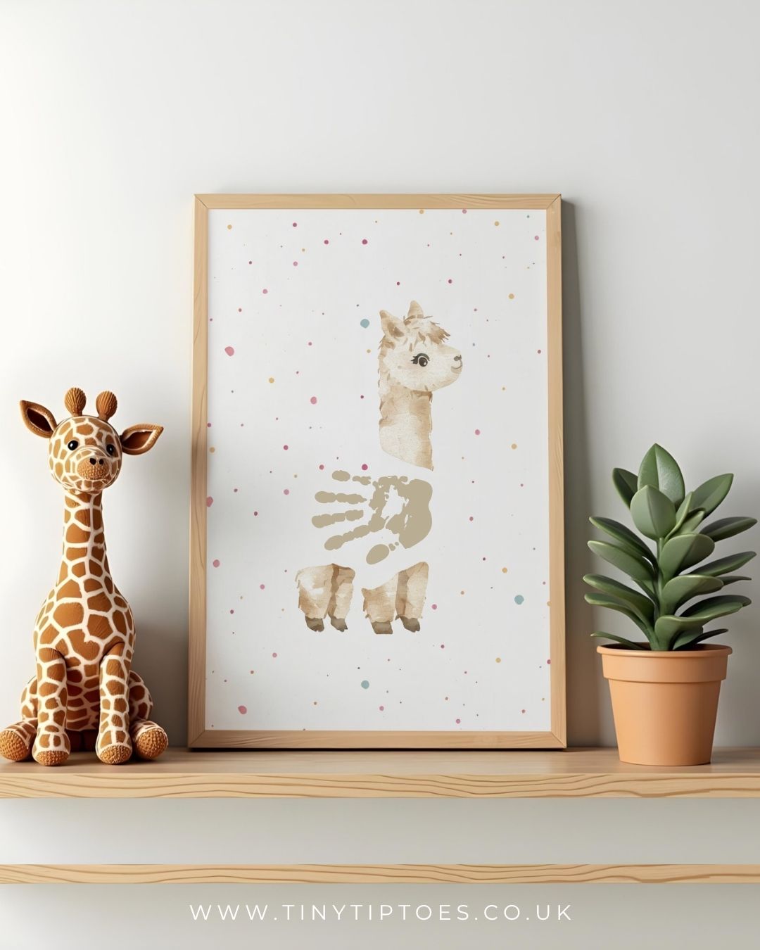 Framed artwork of an alpaca with a handpint body, with colorful dots on a shelf with a toy giraffe and plant.