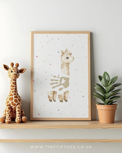 Framed artwork of an alpaca with a handpint body, with colorful dots on a shelf with a toy giraffe and plant.