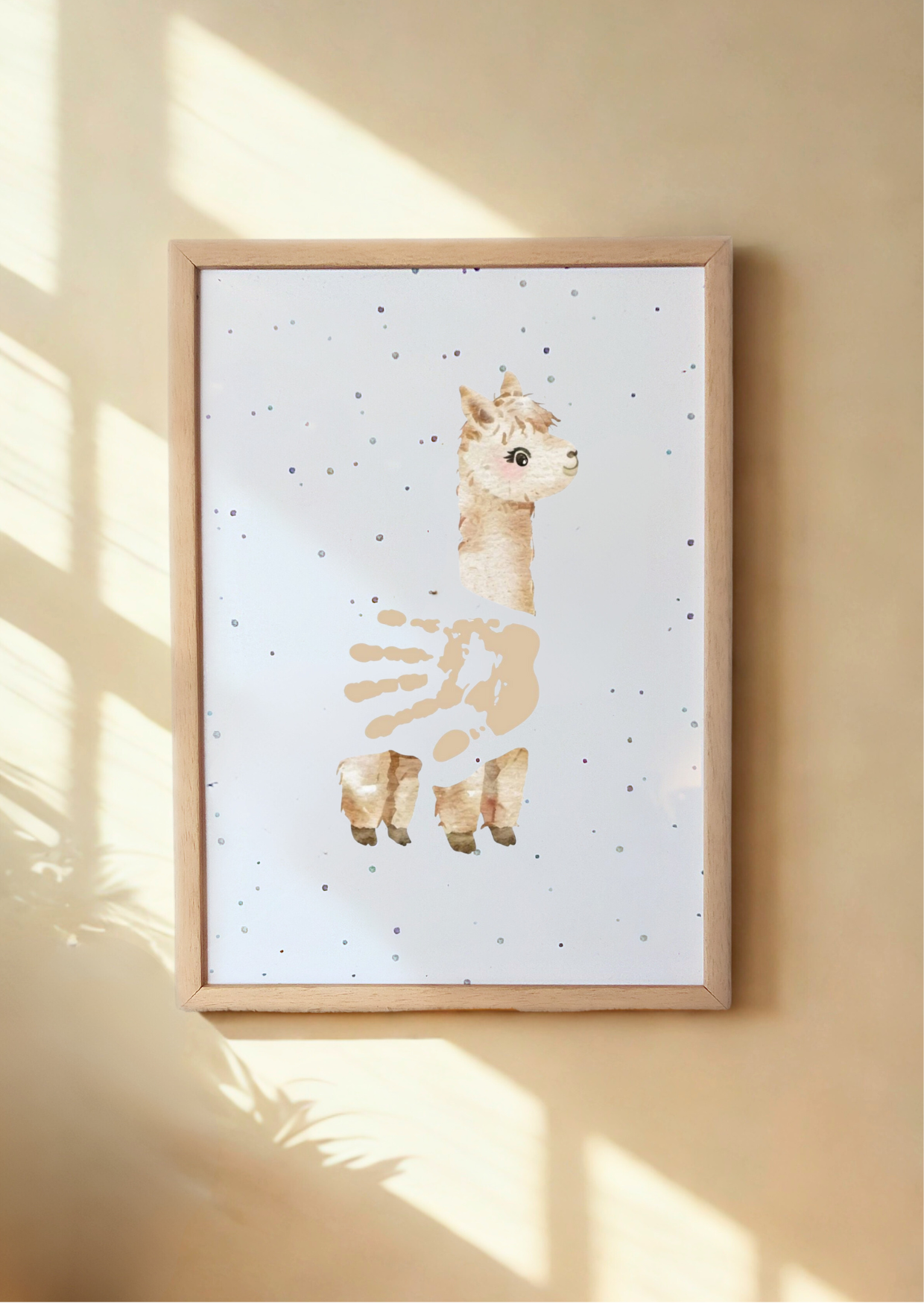 Framed artwork of an alapca with a handprint body on a light background, hanging on a wall.
