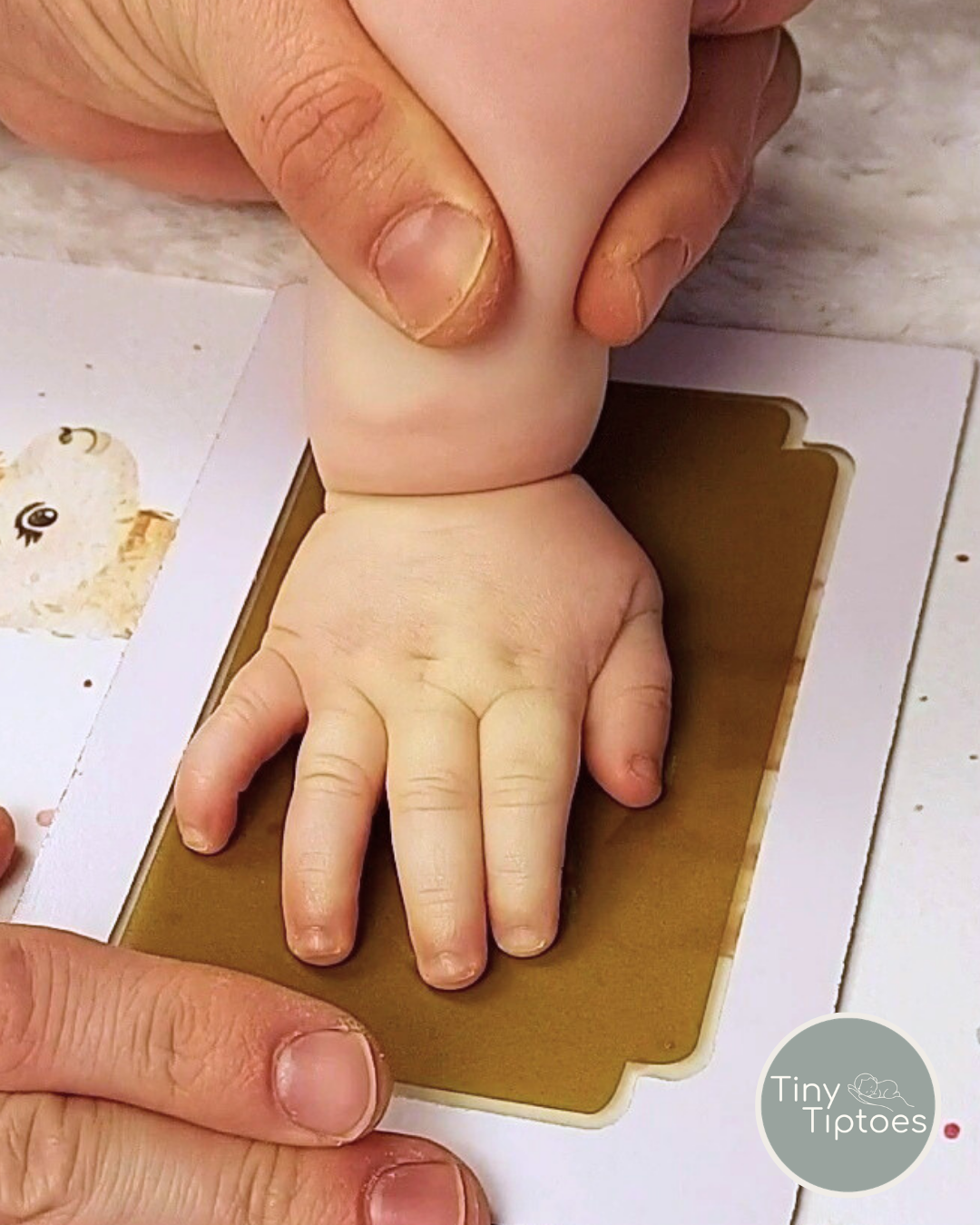 Baby hand print being made on a clean touch ink pad with 'Tiny Tiptoes' branding.