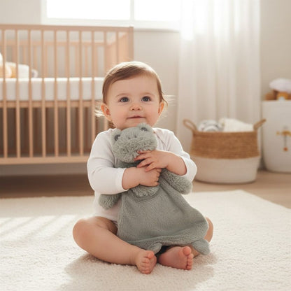 Baby sitting on a rug holding a soft toy frog comforter in a nursery