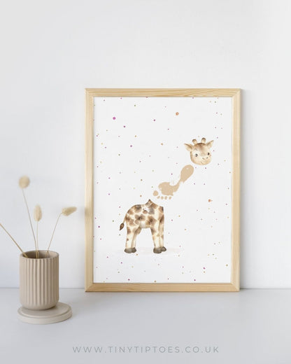 Framed artwork of a giraffe with a footprint neck on a white wall with a vase and dried plants.