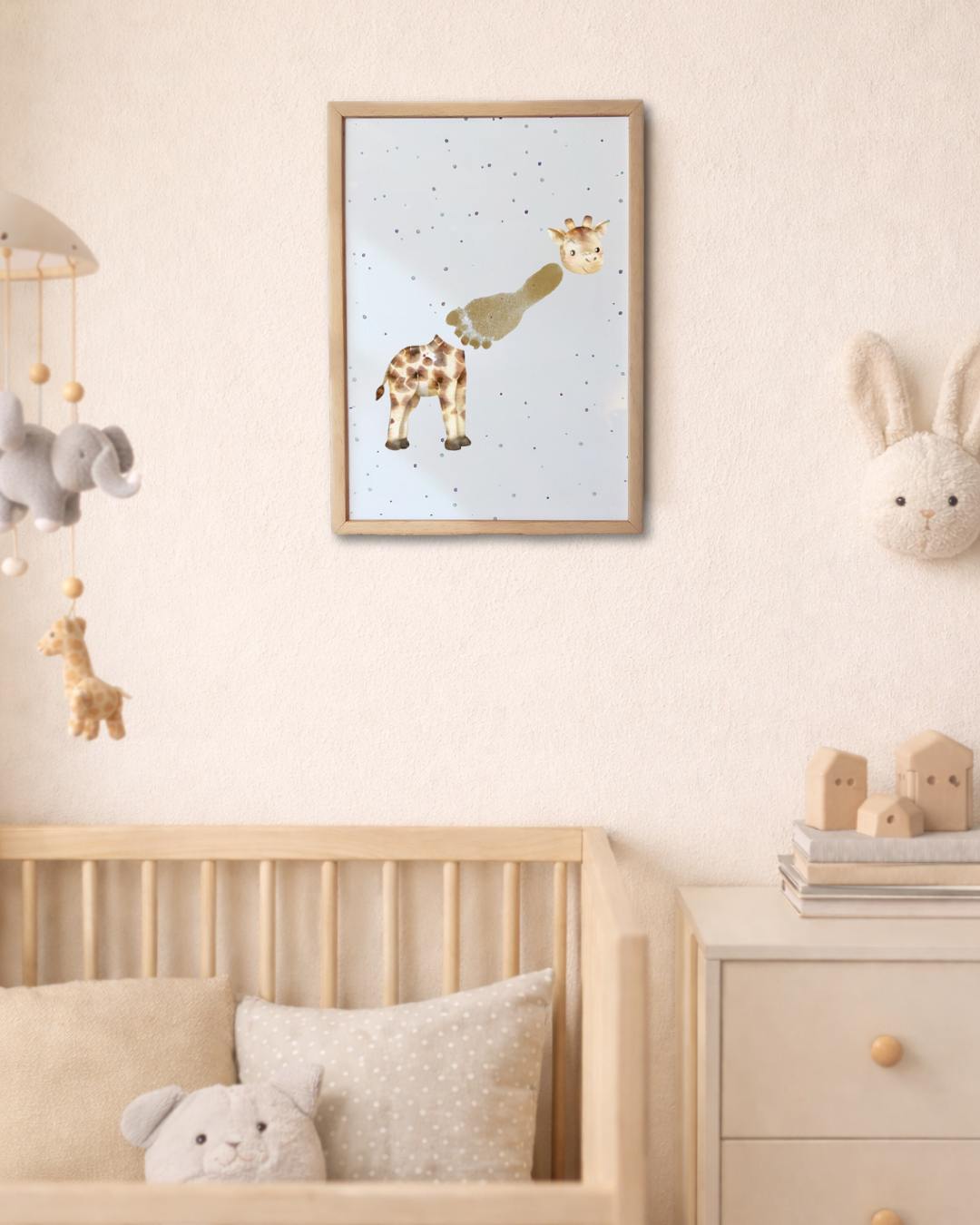 Nursery room with a framed picture of a giraffe, crib, and toys. giraffe's neck is made from a baby's footprint
