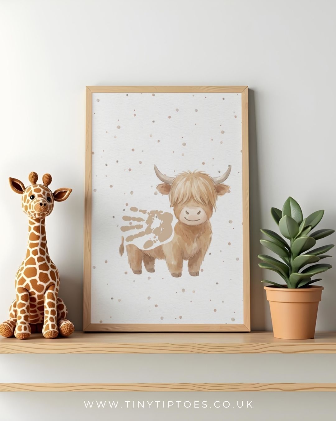Framed artwork of a highland cow with a handprint body with a toy giraffe and plant on a shelf.