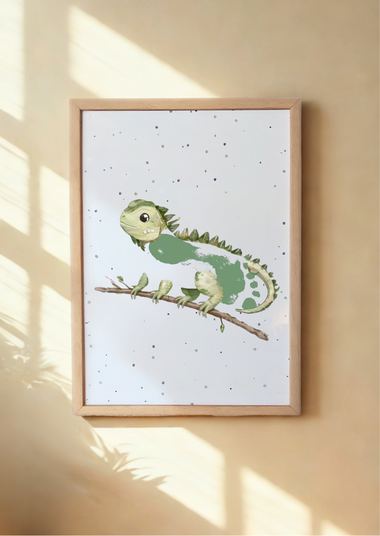 Framed illustration of a green iguana with a baby's footprint as it's body on a branch against a light background 