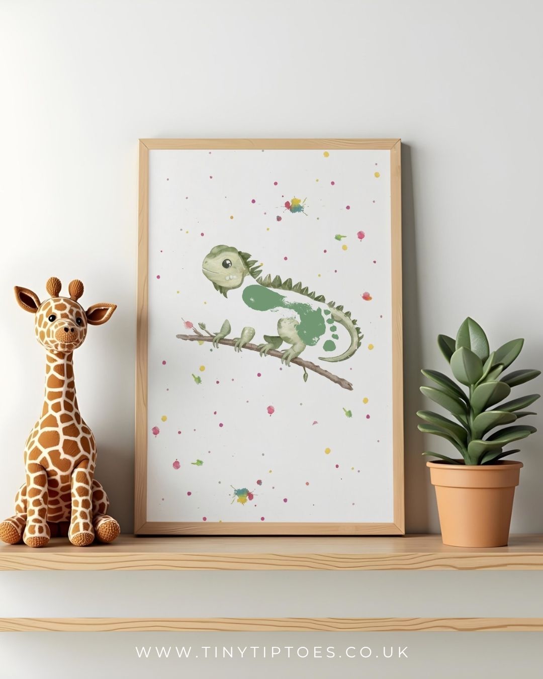 Framed children's illustration of a green iguana with a footprint body on a branch with a stuffed giraffe and potted plant on a shelf.