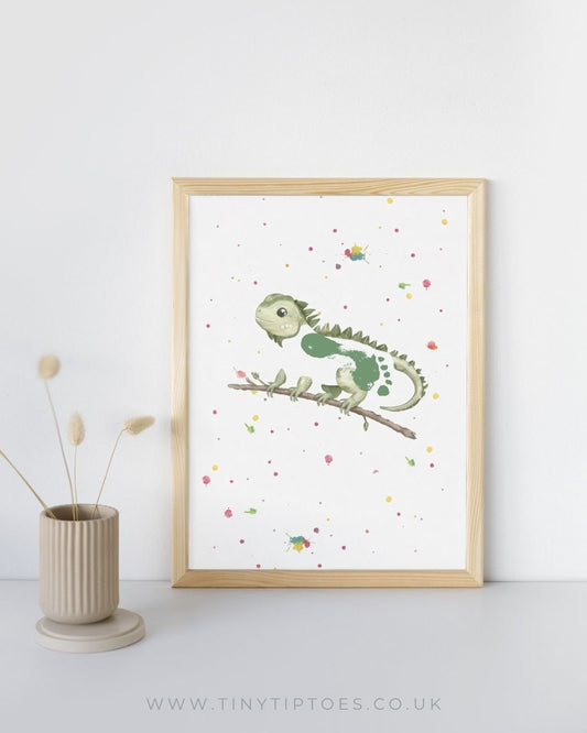 Framed artwork of a green iguana with a footprint bodt on a branch with colorful dots, placed on a white surface with a light background.