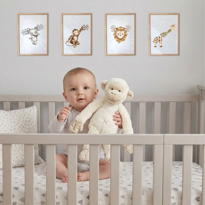 Baby sitting in a crib cot holding a plush toy, with framed animal prints on the wall with baby handprints and footprints