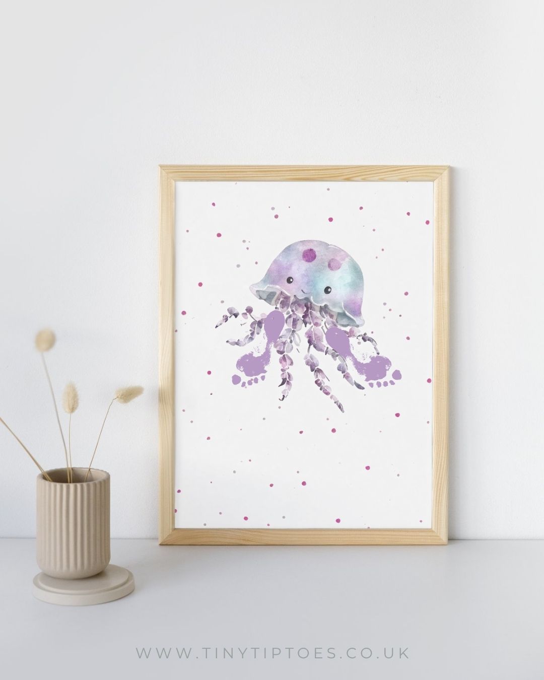 Framed artwork of a purple jellyfish with footprint tentacles on a white background with polka dots, next to a vase with dried plants.