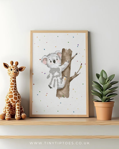 Framed artwork of a koala with handprint body on a tree branch with a toy giraffe and plant on a shelf.
