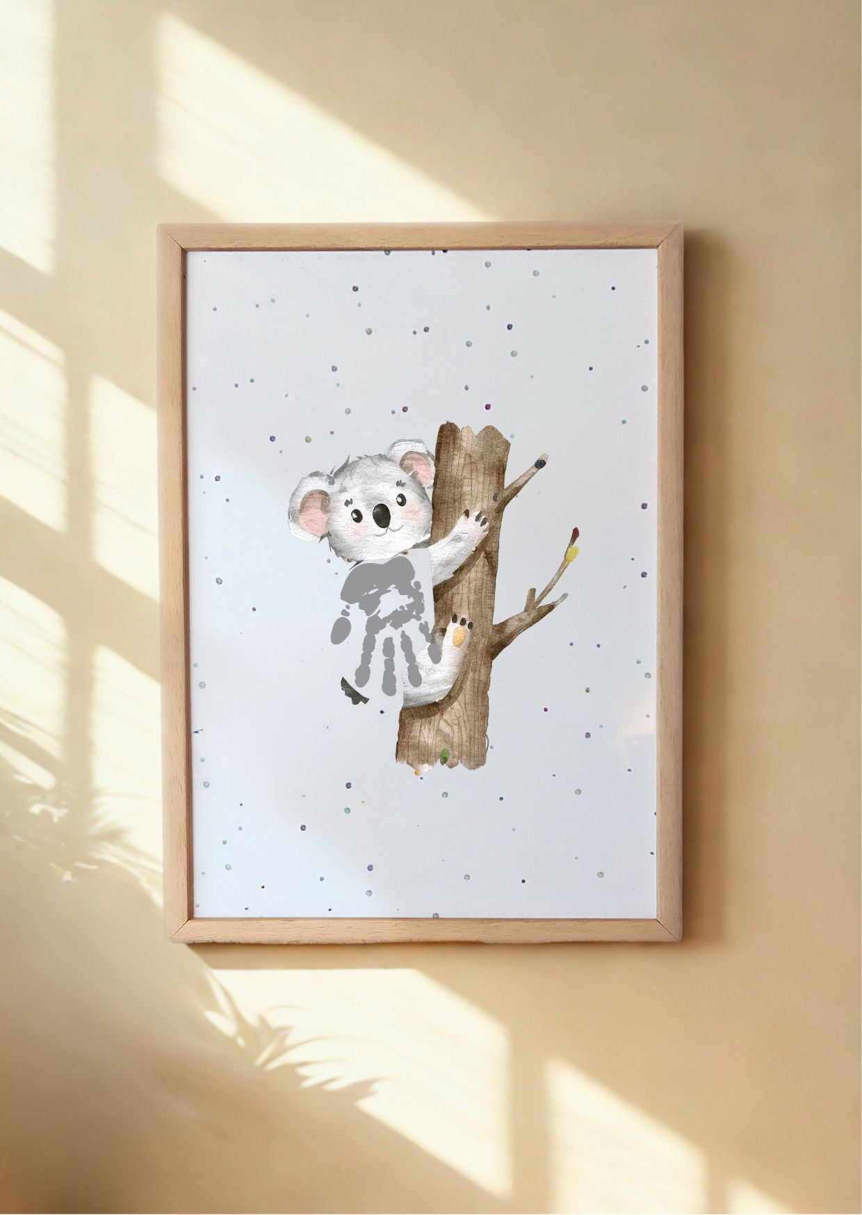 Framed artwork of a koala on a branch with a baby's handprint, on a beige wall.