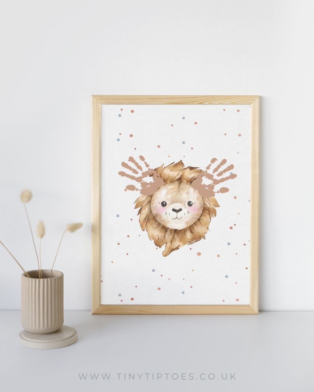 Framed artwork of a lion's face with handprint ears on a white background with a vase on a shelf.