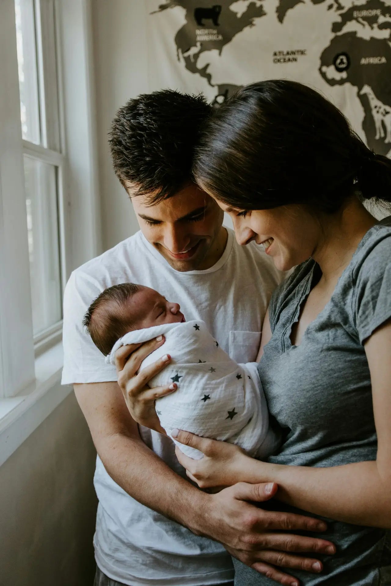Mum and Dad holding newborn swaddled baby and smiling