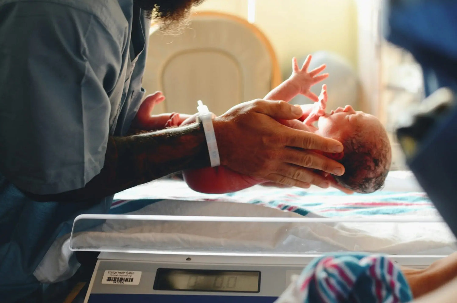 Newborn Baby being held above Hospital Scales by a nurse or midwife