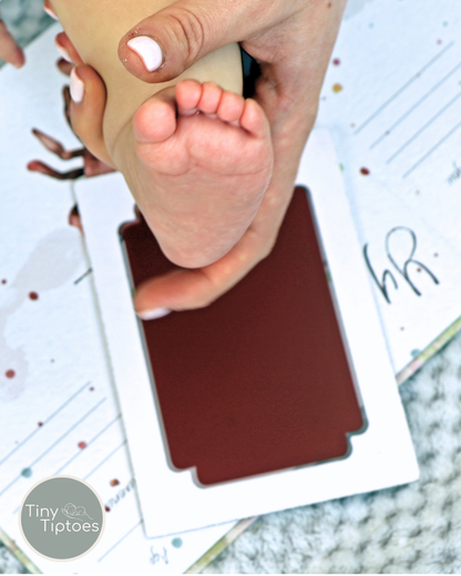 Baby footprint being made on a red mess free, clean touch ink pad with 'Tiny Tiptoes' branding.