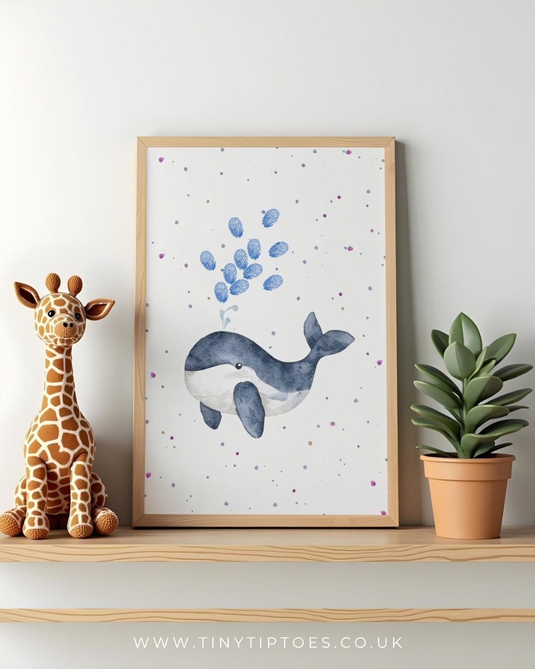 Framed artwork of a whale with fingerprint bubbles on a shelf with a toy giraffe and plant.