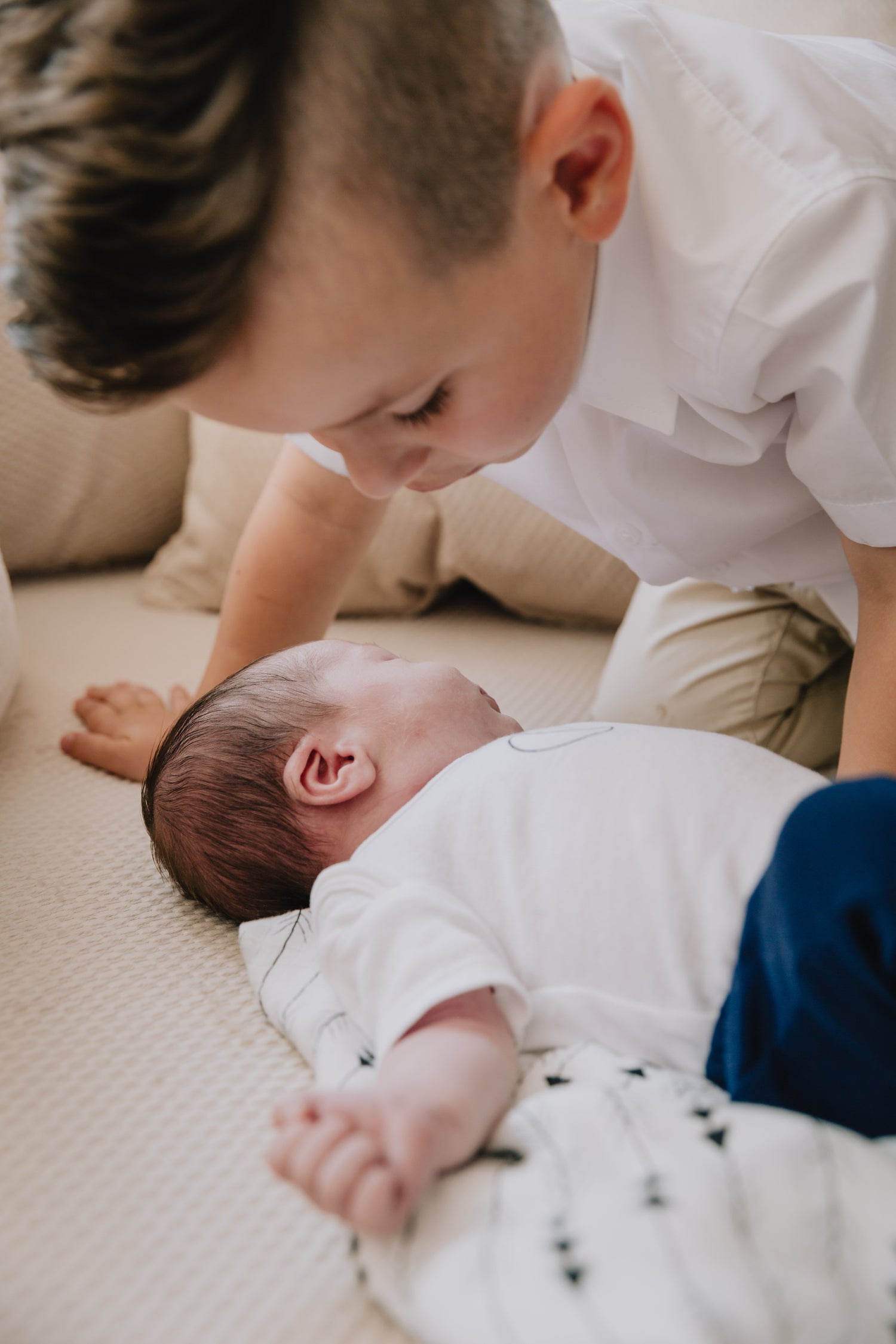 baby and older brother lying on a blanket looking at each other