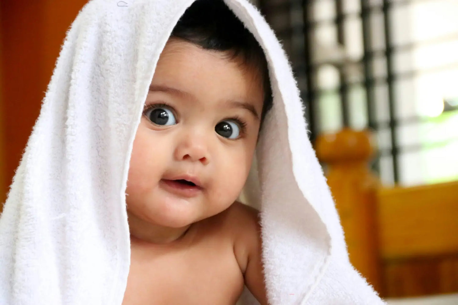 baby with bath towel over his head. Large dark eyes