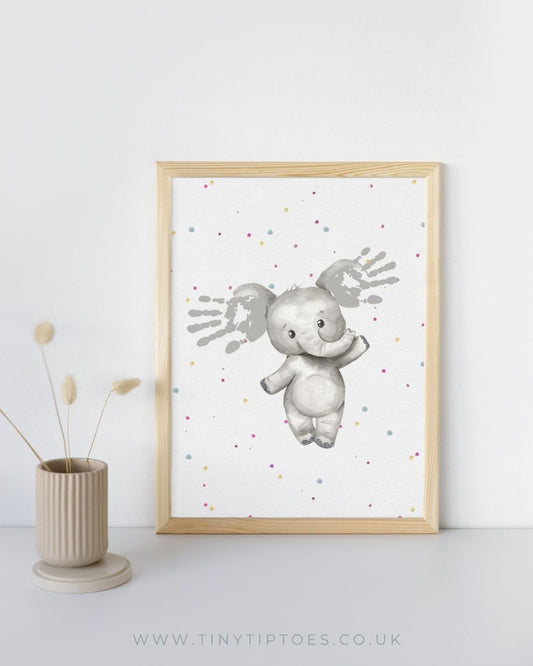 Framed print of an elephant with handprint ears on a white background, displayed on a shelf.