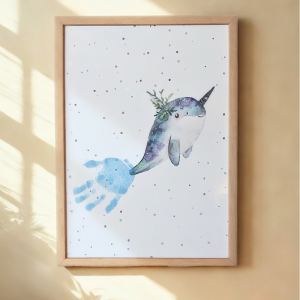 A framed print of narwhal with a child's handprint for its tail
