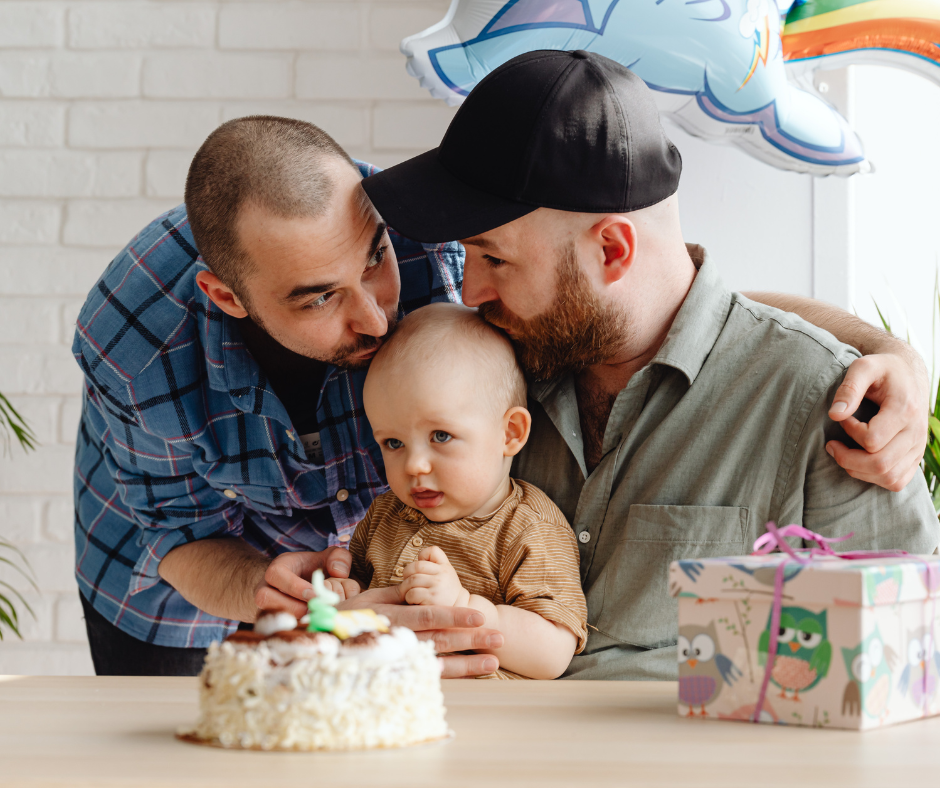 Two fathers celebrating baby’s first birthday with cake – family milestone moment and meaningful baby memory keepsake concept