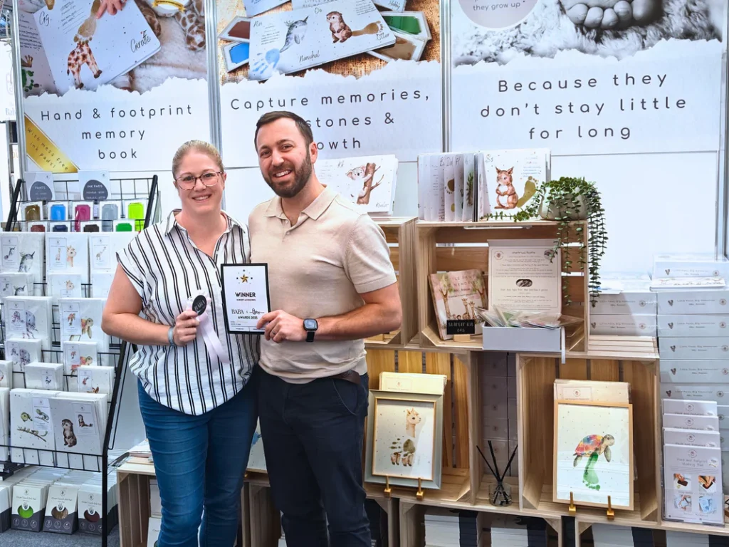 Co-founders of Tiny Tiptoes standing at their stand at the baby show, holding the award winners badge